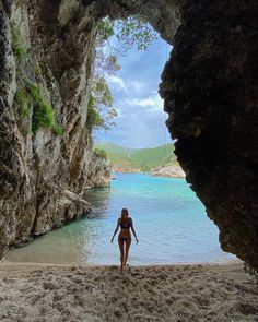 a woman standing on the beach in front of an ocean cave with blue water and cliffs