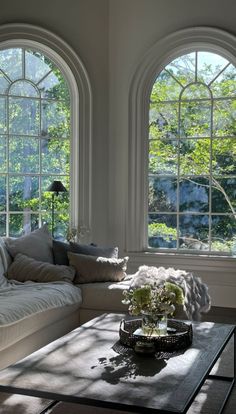 a living room filled with furniture and two large windows covered in sun shining through them