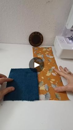 two hands are working on an orange and blue piece of fabric next to a sewing machine