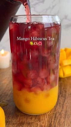 a person pouring tea into a glass on top of a wooden table next to sliced mangoes