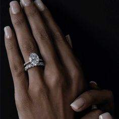 a woman's hand with two rings on her fingers and the other hand holding an engagement ring