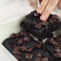 a person picking up some brownies in a white bowl with chocolate chips on top