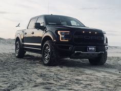 a black truck parked on top of a sandy beach