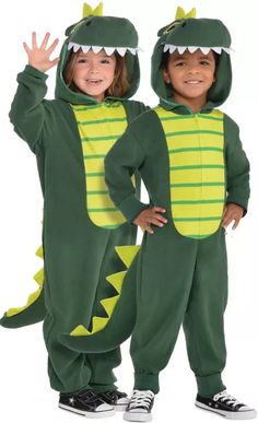 two children in dinosaur costumes standing next to each other, one holding his hand up