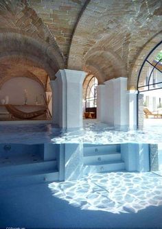 an indoor swimming pool with stone walls and arches in the center, surrounded by water features