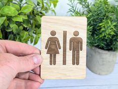 a person holding up a wooden sign with a man and woman on it in front of some potted plants