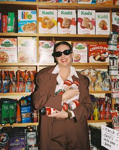 a woman holding a baby standing in front of a store shelf filled with cereals