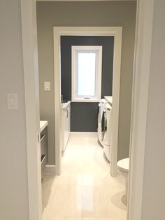 an empty bathroom with toilet, sink and washer dryer in the doorway leading to another room