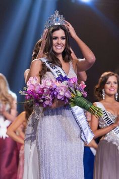 a woman in a dress and crown holding flowers on her head while standing next to other women