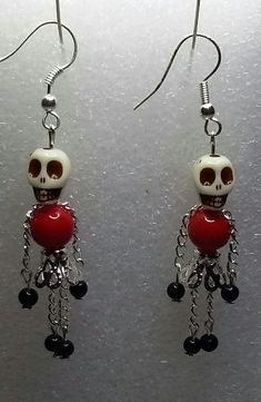 a pair of red and white skull earrings with chains hanging from it's earwires