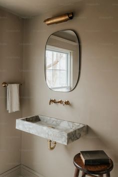 a white sink sitting under a mirror next to a wooden stool in a bath room