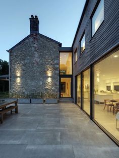 an outdoor patio with tables and benches next to a stone building at dusk, lit by lights on the windows