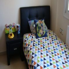 a bed with colorful sheets and pillows in a room next to a small black table