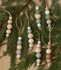 several wooden beads hanging from a tree branch with pine needles and twine on it