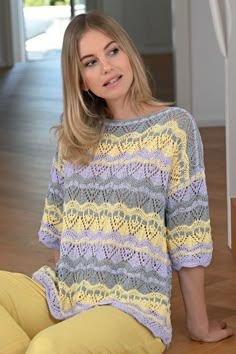 a woman is sitting on the floor wearing yellow pants and a colorful knitted sweater