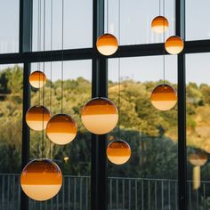 several balls hanging from the ceiling in front of large windows with trees and hills behind them