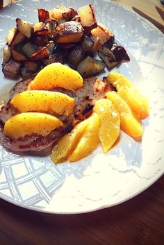 a white plate topped with meat covered in mango slices and sliced up potatoes on top of it