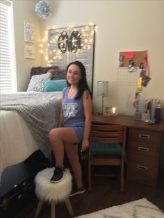 a woman sitting on top of a bed next to a white fur footstool