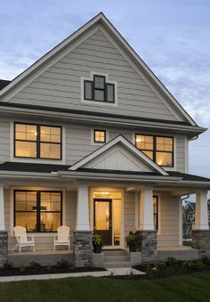 a house with two white chairs sitting on the front porch and windows lit up at night