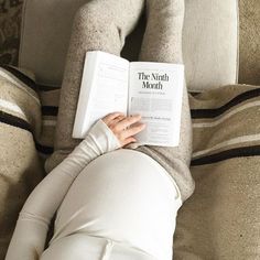 a woman laying down reading a book on her stomach while wearing leggings and socks