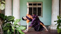 a woman is doing yoga in front of a building with columns and plants on the ground