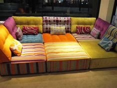 a multicolored couch sitting in front of a window with lots of pillows on it