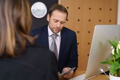 a man in a suit is looking at his cell phone while sitting at a desk