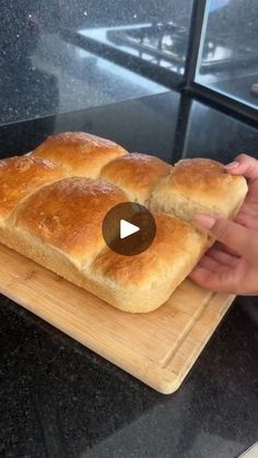 a person holding a loaf of bread on top of a wooden cutting board