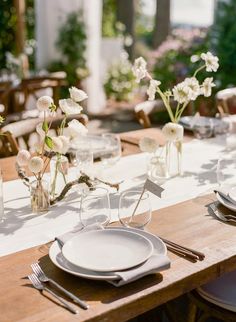 the table is set with plates, silverware and vases filled with white flowers