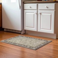 a kitchen with white cabinets and wood floors, including a rug on the floor in front of the refrigerator