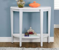 a white table with an orange vase on top and a rug in front of it