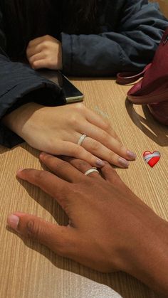 two people sitting at a table with their hands on each other's fingers,