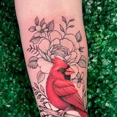 a red bird sitting on top of a tree branch with flowers in it's beak