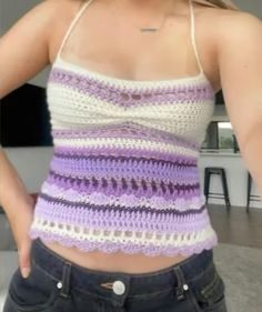 a woman wearing a purple and white crochet top with her hands on her hips