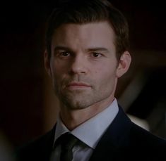 a close up of a person wearing a suit and tie in a dark room with one eye open