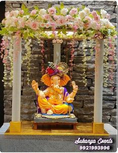 a statue of the god ganesh in front of a stone wall with flowers on it