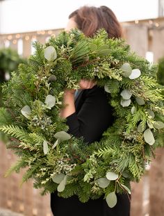 a woman holding a wreath with greenery on it