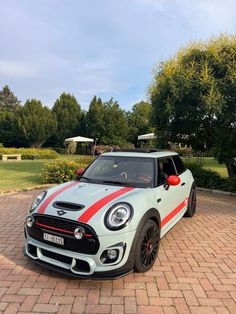 a white and red car parked on top of a brick road next to some trees