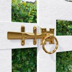 a close up of a door handle on a white fence with green bushes in the background