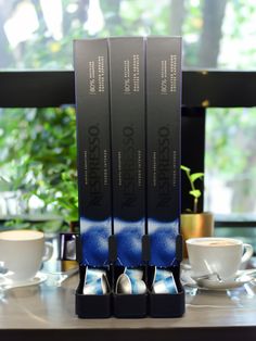 three coffee cups sitting on top of a table next to two black and white boxes