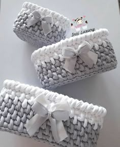 three knitted baskets with white bows on the top and one has a bow at the bottom