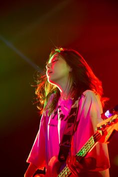 a woman with long hair playing a guitar in front of a microphone and some lights