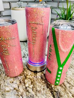 three pink glitter tumblers sitting on top of a counter next to a potted plant