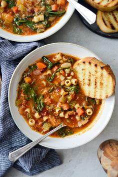 two bowls of vegetable soup with bread on the side