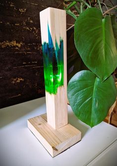 a green and blue vase sitting on top of a wooden stand next to a leafy plant