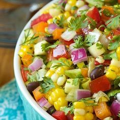 a bowl filled with corn and vegetables on top of a blue table cloth next to a fork