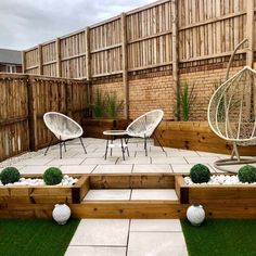 an outdoor patio with chairs and plants in the grass, next to a wooden fence