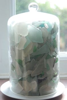 there is a glass jar with sea glass in it on the table next to a window