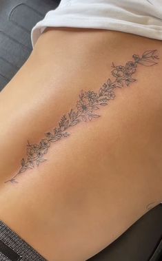 a woman's lower back tattoo with flowers on her left side ribcage