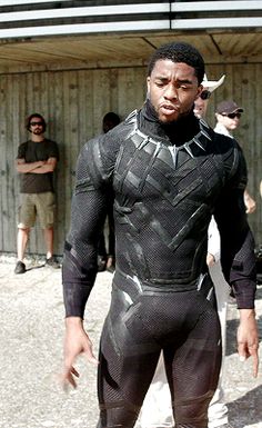 a man dressed as black panther standing in front of a building with other people behind him